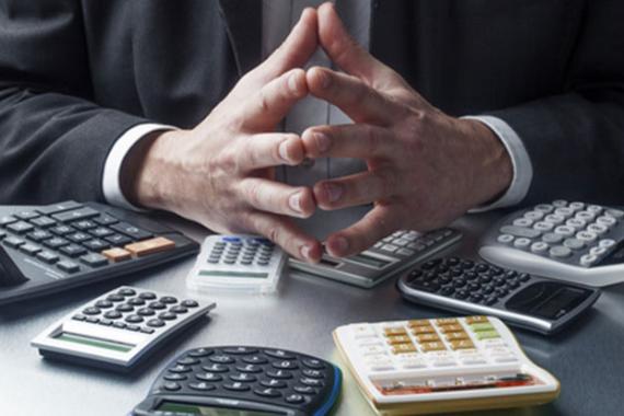 Homme se tenant assis les mains jointes devant plusieurs machines à calculer