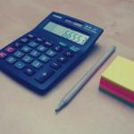 Une calculatrice, un stylo à bille et un bloc notes posés sur un bureau