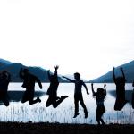 Groupe de jeunes (silhouettes) en train de sauter en l'air devant une étendue d'eau